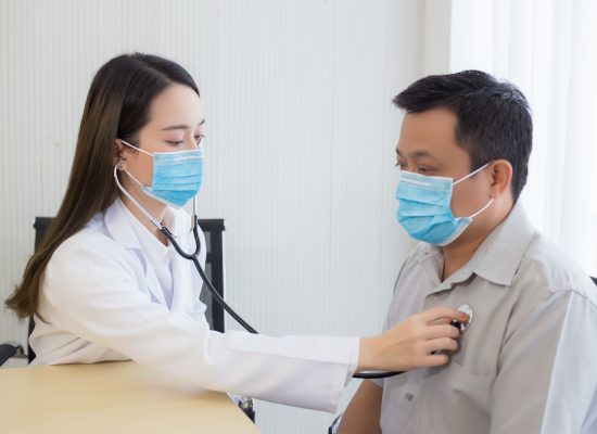 Asian man patient are checked up his health while a woman doctor use a stethoscope to hear heart rate of hims in Coronavirus pandemic. Coronavirus protection concept.